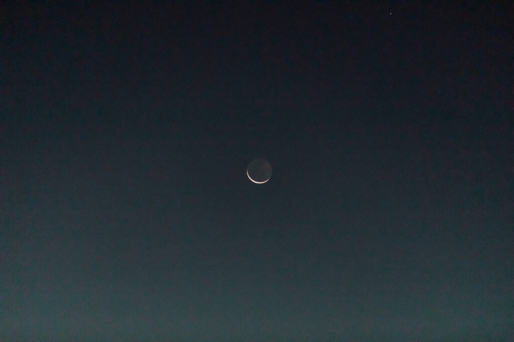 The moon visible above the desert canyon during sunrise elopement