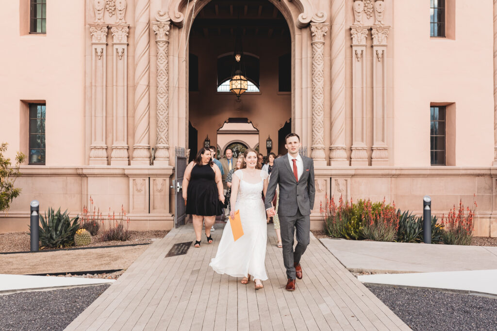 Bride and groom walking to ceremony spot with guests at pima county historic courthouse