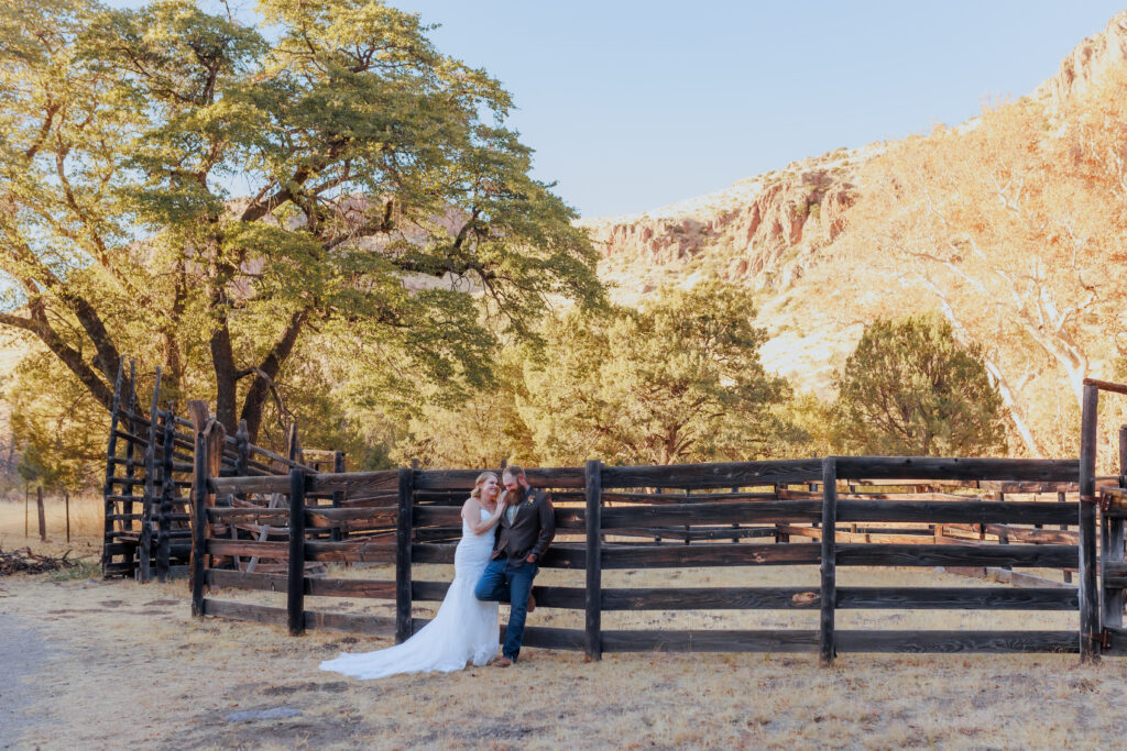 bride and groom on fence at historic faraway ranch in arizona