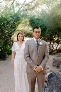 Close-up of a bride placing her hand on her groom’s shoulder during their first look in the lush desert gardens of Westin La Paloma.