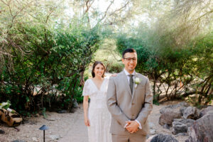 The bride and groom share a joyful moment during their first look, with the groom smiling broadly against the green desert backdrop of Westin La Paloma.