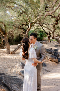 The bride and groom share a romantic kiss on a shaded desert trail, surrounded by the natural beauty of the Westin La Paloma grounds.