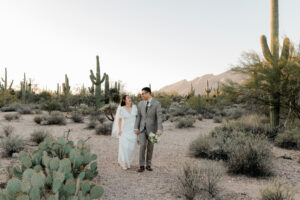 A wide view of the couple walking away from the camera on a sandy trail, highlighting the sprawling desert landscape of Sabino Canyon.