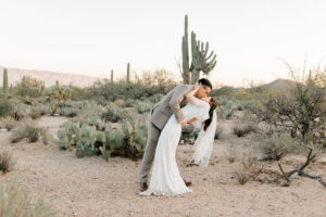 The groom playfully dips the bride back for a kiss on a desert trail in Sabino Canyon after their getting-ready session at Westin La Paloma.
