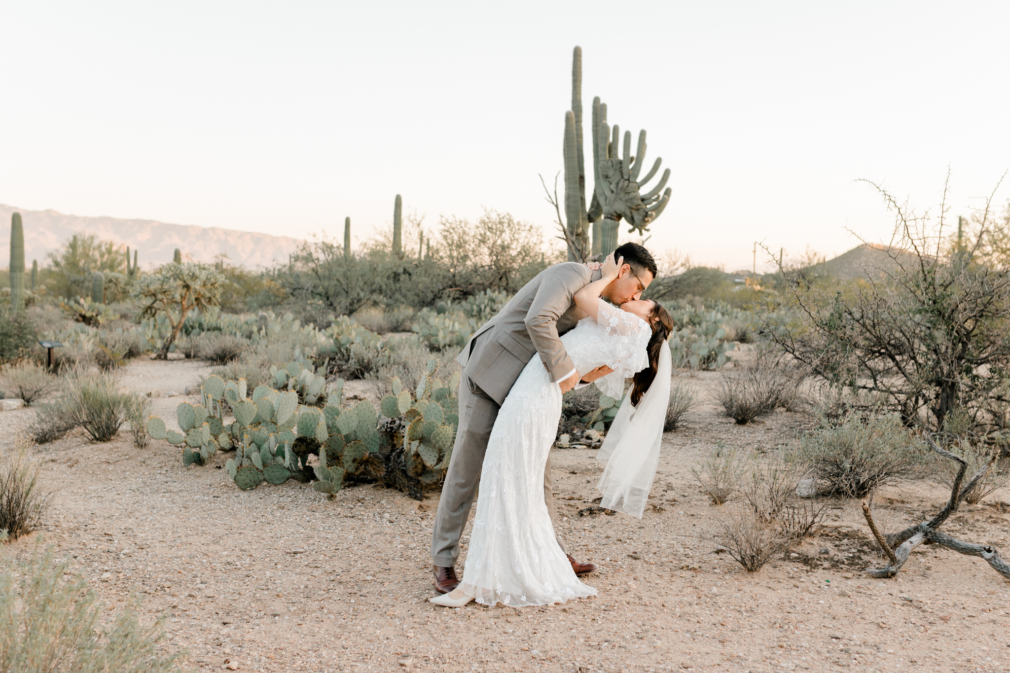 The groom playfully dips the bride back for a kiss on a desert trail in Sabino Canyon after their getting-ready session at Westin La Paloma.