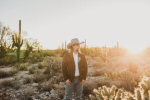 groom standing int he desert at golden hour looking at his new bride.