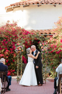 bride and groom first kiss during wedding ceremony at garden venue with pink bougainvillea's behind them