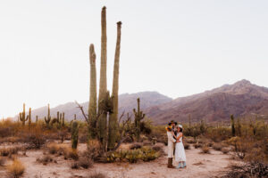 bride and groom pose in desert during blue hour next to tall saguaros