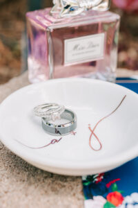 Wedding rings and diamond engagement ring stacked on a monogrammed ceramic ring dish with Miss Dior perfume, Buttes at Reflections wedding venue, Tucson Arizona