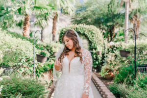 Bride in long-sleeve lace wedding gown looking down with veil blowing in garden at Buttes at Reflections Tucson Arizona, documentary wedding photography