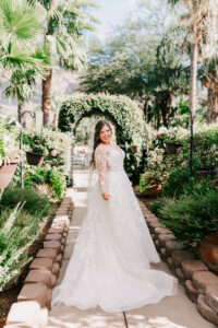 Bride in lace ball gown spinning and smiling on garden path with floral arch and palm trees at Buttes at Reflections wedding venue Tucson Arizona