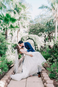 groom dipping bride in long sleeve wedding gown in garden walkway at a tucson wedding venue