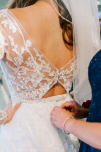 Close-up detail of lace back wedding gown with V-back cutout and beaded waist being fastened by a bridesmaid, Tucson wedding photographer Anita McLeod Photography