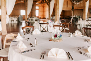 Reception tables set with white linens and burgundy rose centerpieces inside the wood-beamed barn at Tanque Verde Ranch