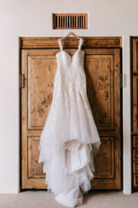 Intricate white lace and tulle mermaid wedding dress hanging on a rustic barn door background.