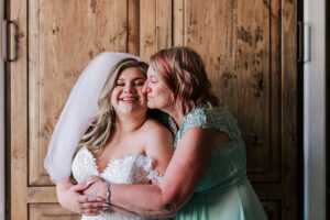Bride laughing as her mother kisses her cheek before the wedding
