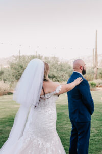Groom waiting outdoors as the bride approaches from behind during their first look at Tanque Verde Ranch