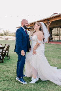 Bride and groom smiling at each other, showing off their custom Converse "Bride" and "Groom" sneakers