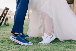 Close-up of the bride's and groom's feet in matching white and navy "Bride" and "Groom" Converse sneakers on the grass