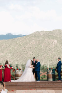 Bride and groom holding hands during their vows on a wooden platform overlooking the Sonoran Desert