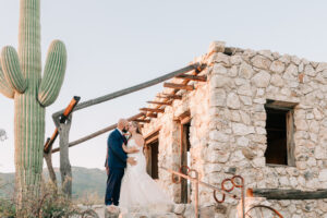 Bride and groom kissing beside a historic stone ruin with a saguaro cactus at Tanque Verde Ranch
